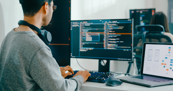 Programador en su escritorio con un portatil y varias pantallas